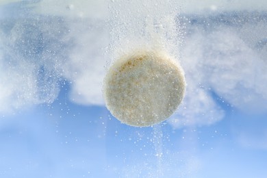 Effervescent pill dissolving in water on light blue background, closeup