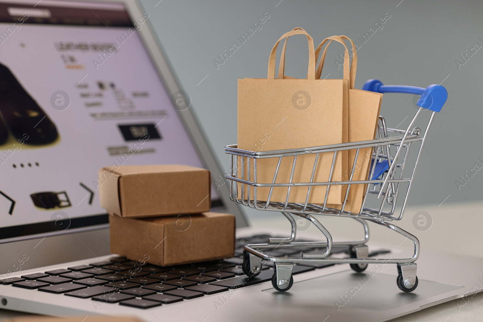 Photo of Mini shopping bags, cart and boxes on laptop against light grey background, closeup. Online store