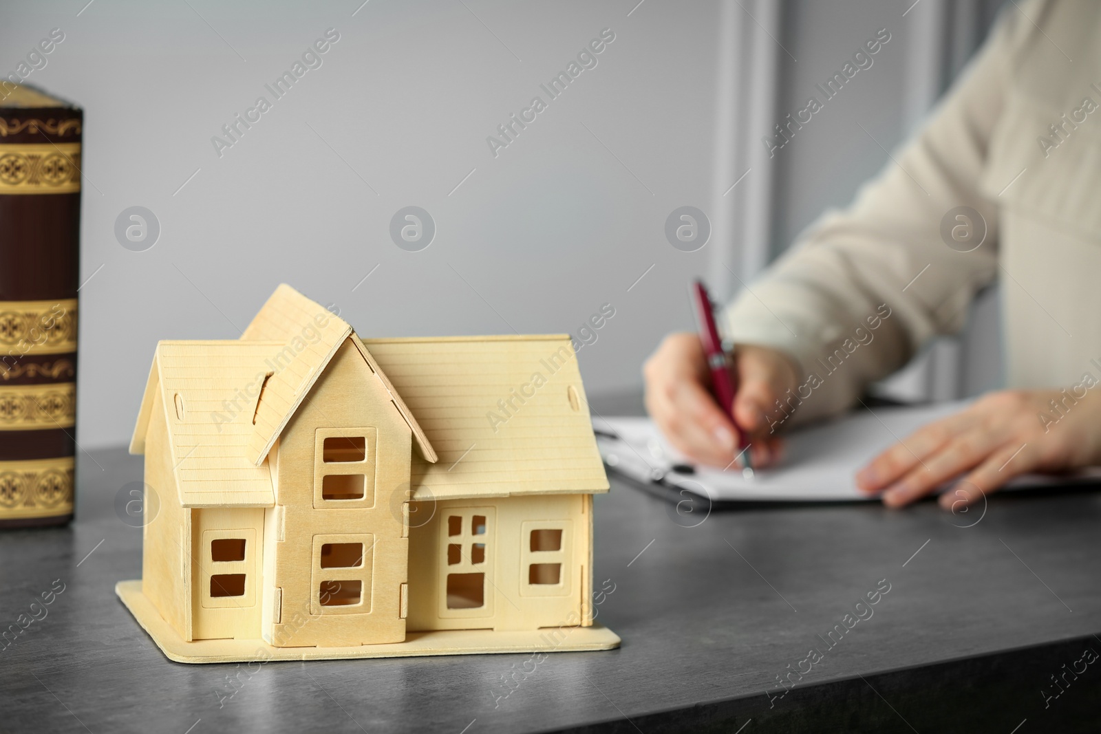 Photo of Construction and land law concepts. Woman writing in clipboard at grey table, focus on house model. Space for text