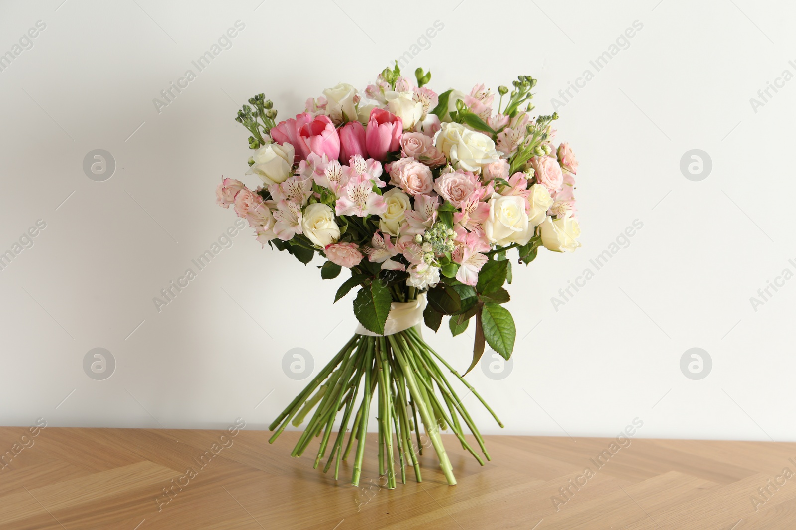 Photo of Beautiful bouquet of fresh flowers on wooden table near white wall