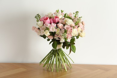 Beautiful bouquet of fresh flowers on wooden table near white wall