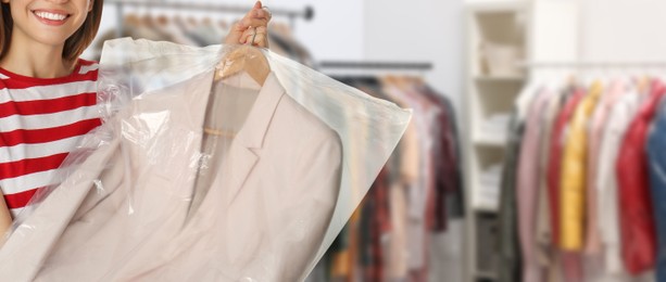 Image of Dry-cleaning service. Woman holding hanger with jacket in plastic bag indoors, space for text. Banner design