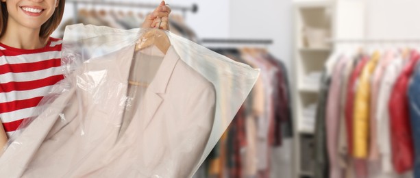 Dry-cleaning service. Woman holding hanger with jacket in plastic bag indoors, space for text. Banner design