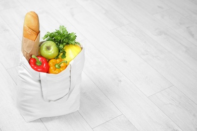 Textile shopping bag full of vegetables with fruits and baguette on floor. Space for text