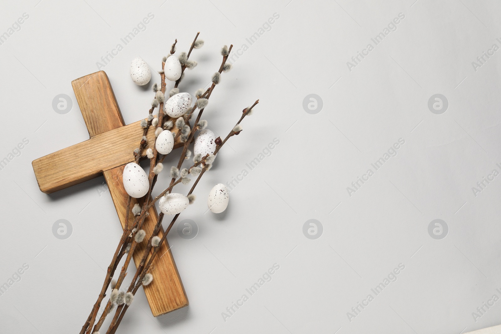 Photo of Wooden cross, painted Easter eggs and willow branches on light grey background, top view. Space for text