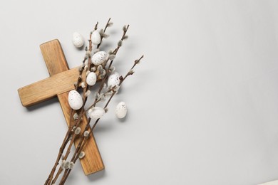 Photo of Wooden cross, painted Easter eggs and willow branches on light grey background, top view. Space for text