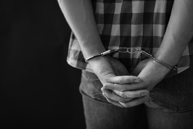 Criminal detained in handcuffs against dark background, space for text. Black and white effect