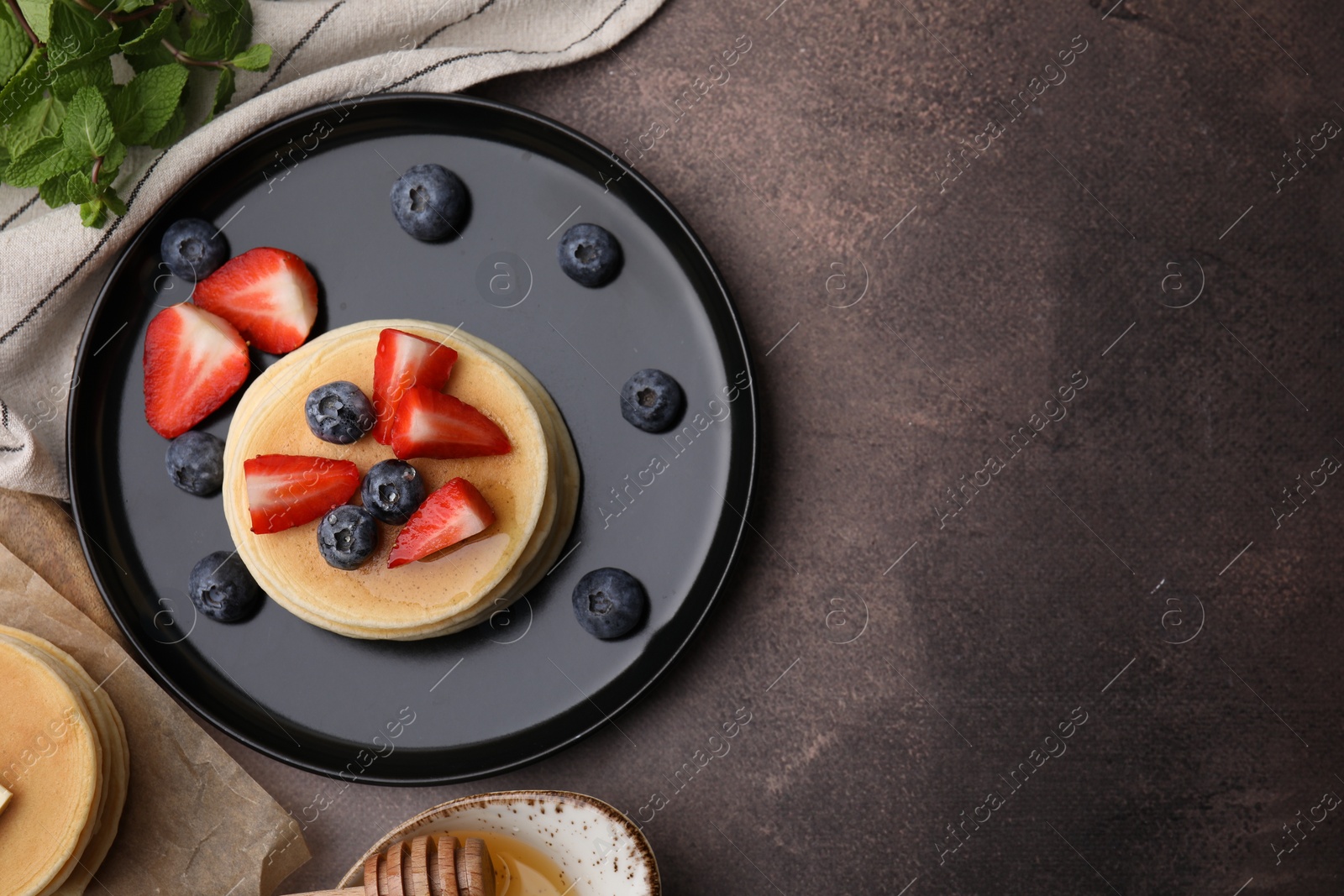 Photo of Delicious pancakes with strawberries and blueberries served on brown textured table, flat lay. Space for text