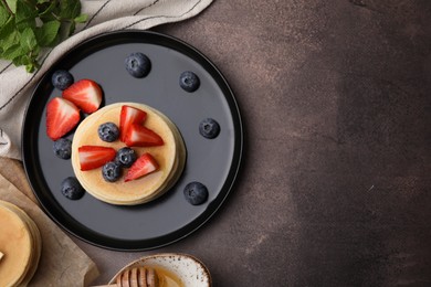 Delicious pancakes with strawberries and blueberries served on brown textured table, flat lay. Space for text