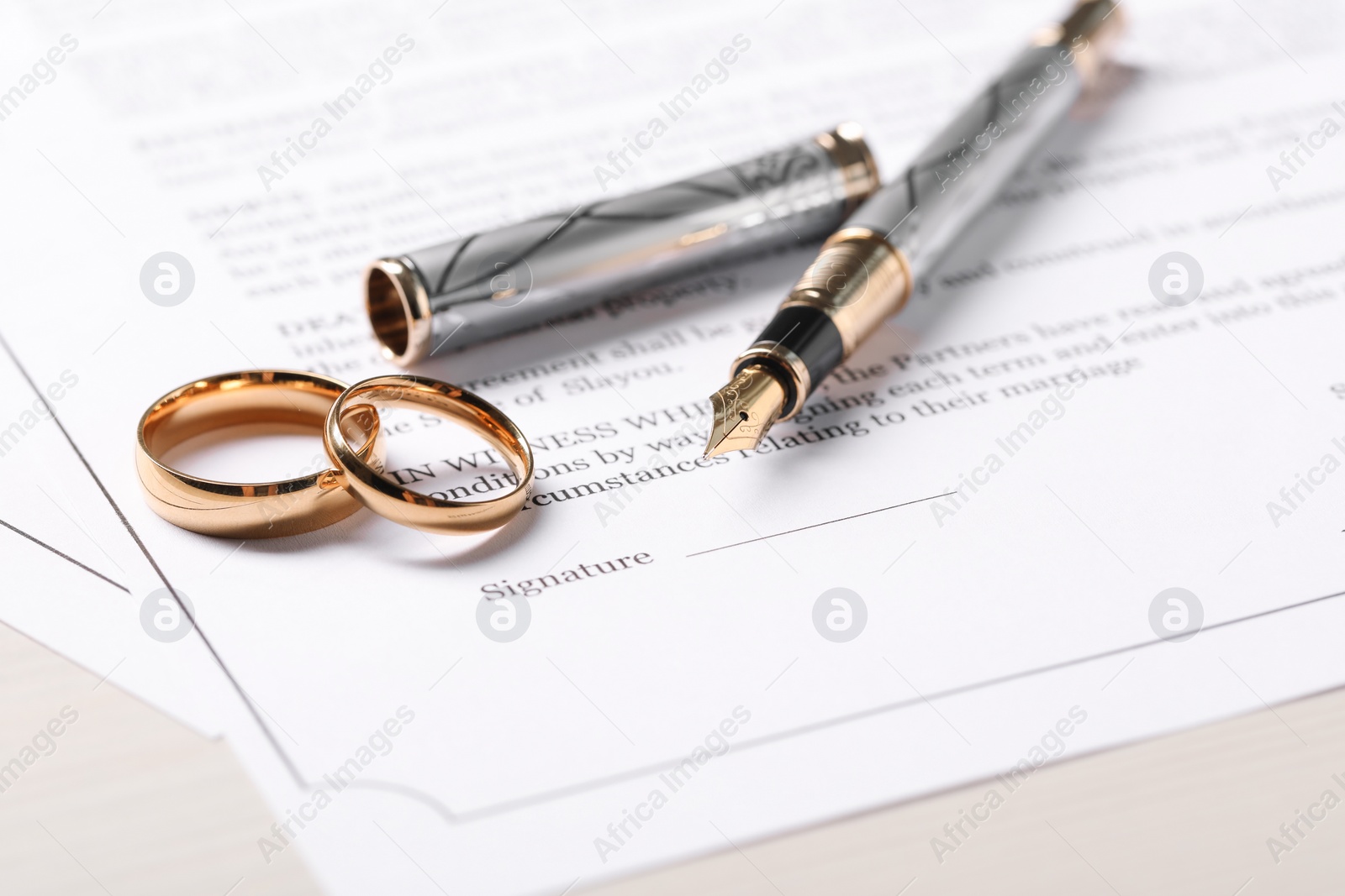 Photo of Marriage contracts, gold rings and pen on light wooden table, closeup