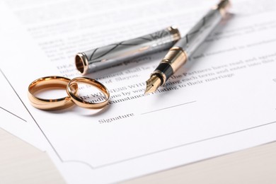 Marriage contracts, gold rings and pen on light wooden table, closeup