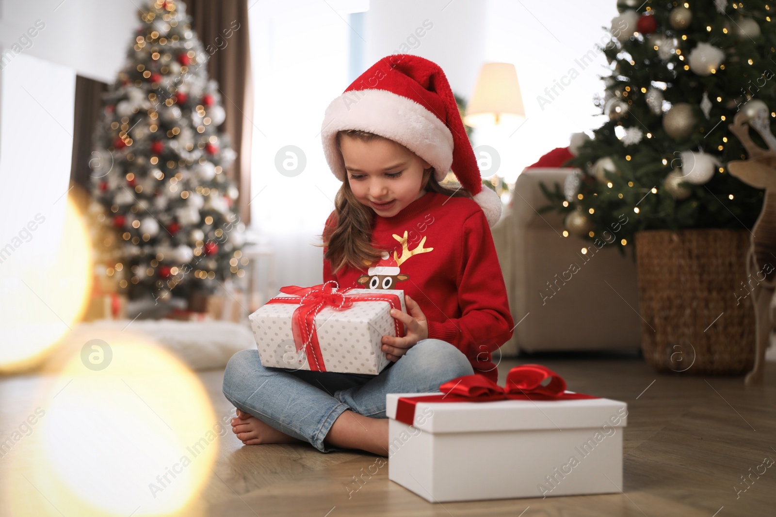 Photo of Cute little girl holding gift box in room decorated for Christmas