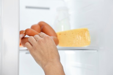 Young woman taking sausages out of refrigerator, closeup