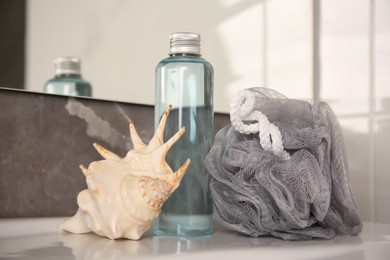 Photo of Grey sponge, seashell and shower gel bottle on washbasin in bathroom