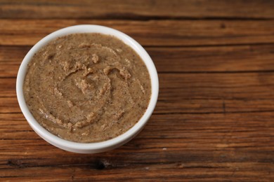 Photo of Delicious nut butter in bowl on wooden table, closeup. Space for text