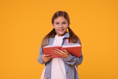 Happy schoolgirl with open book on orange background