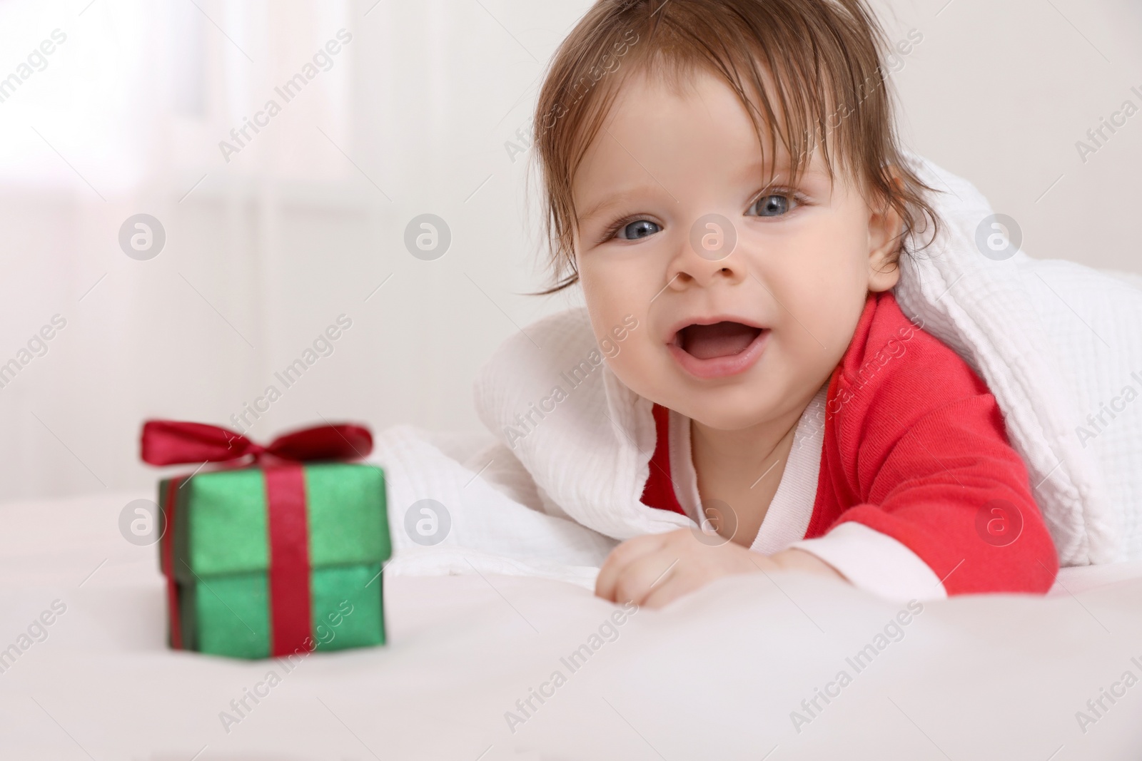 Photo of Cute baby wearing festive Christmas costume with gift box in crib, closeup