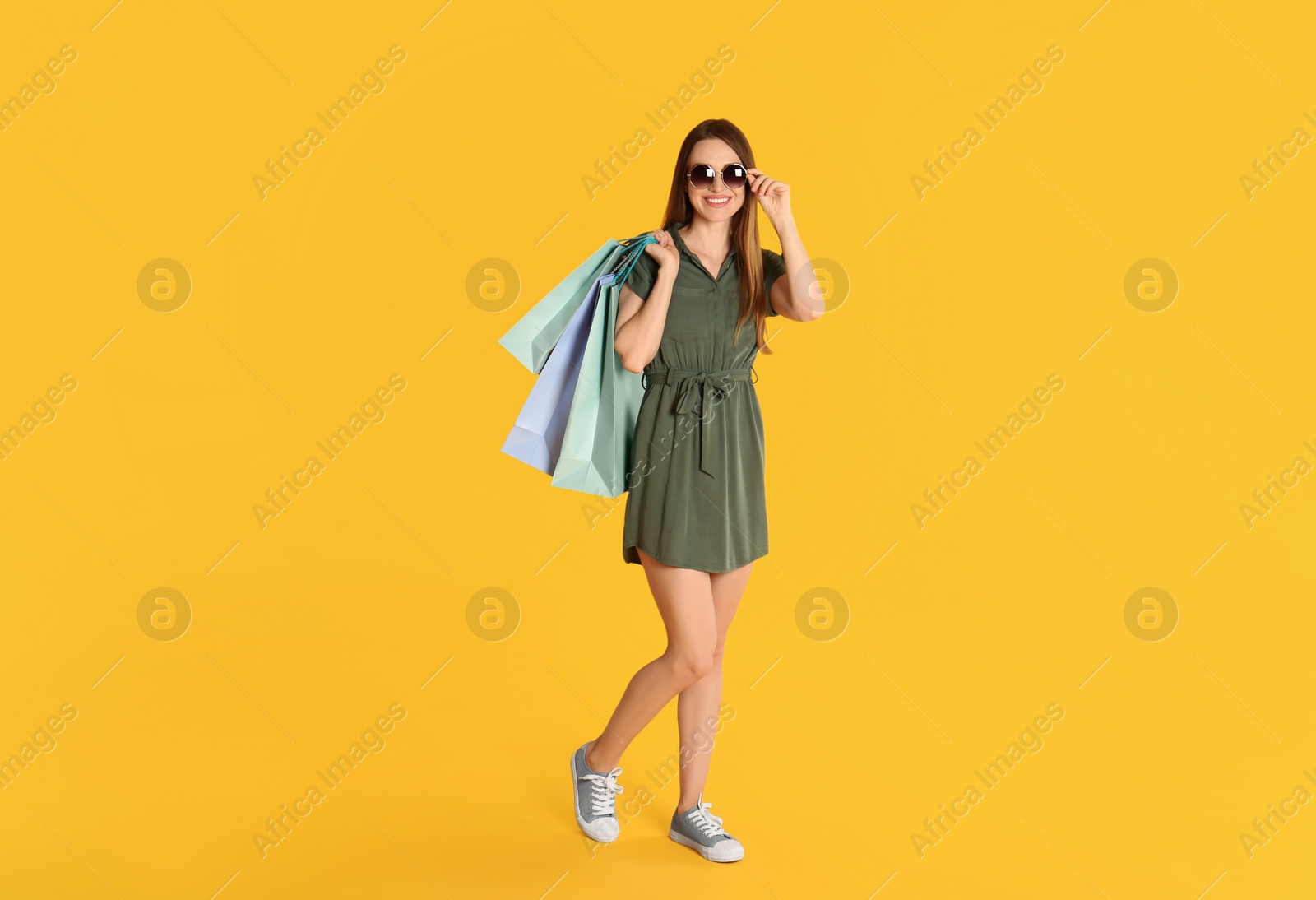 Photo of Beautiful young woman with paper shopping bags on yellow background