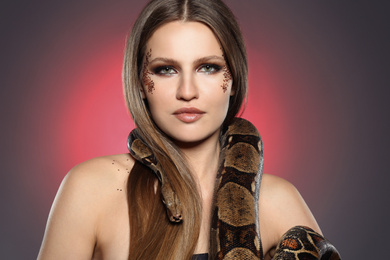 Photo of Beautiful woman with boa constrictor on color background