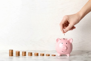 Photo of Woman putting coin into piggy bank against light background. Space for text