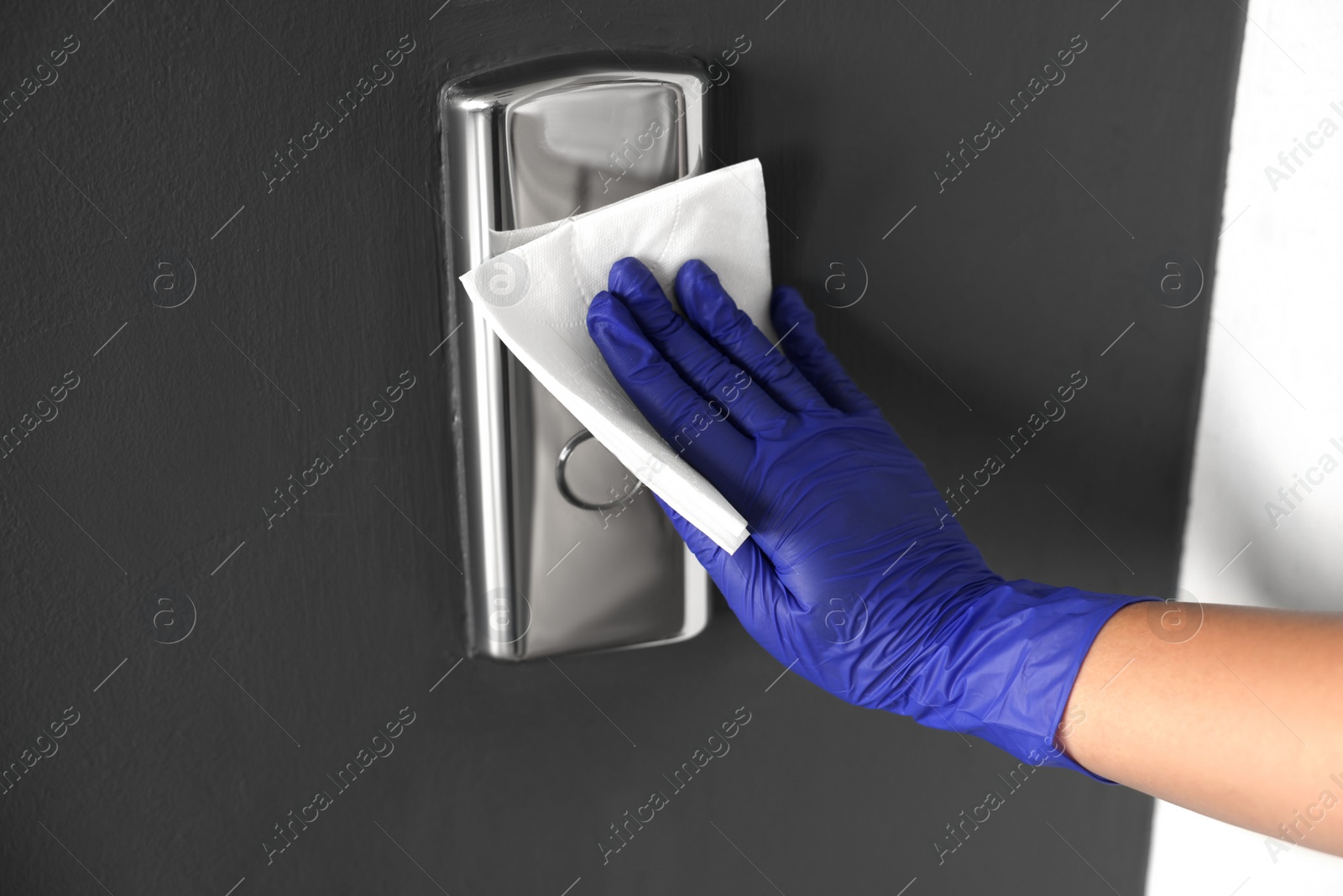 Photo of Woman wiping elevator call panel with paper napkin, closeup