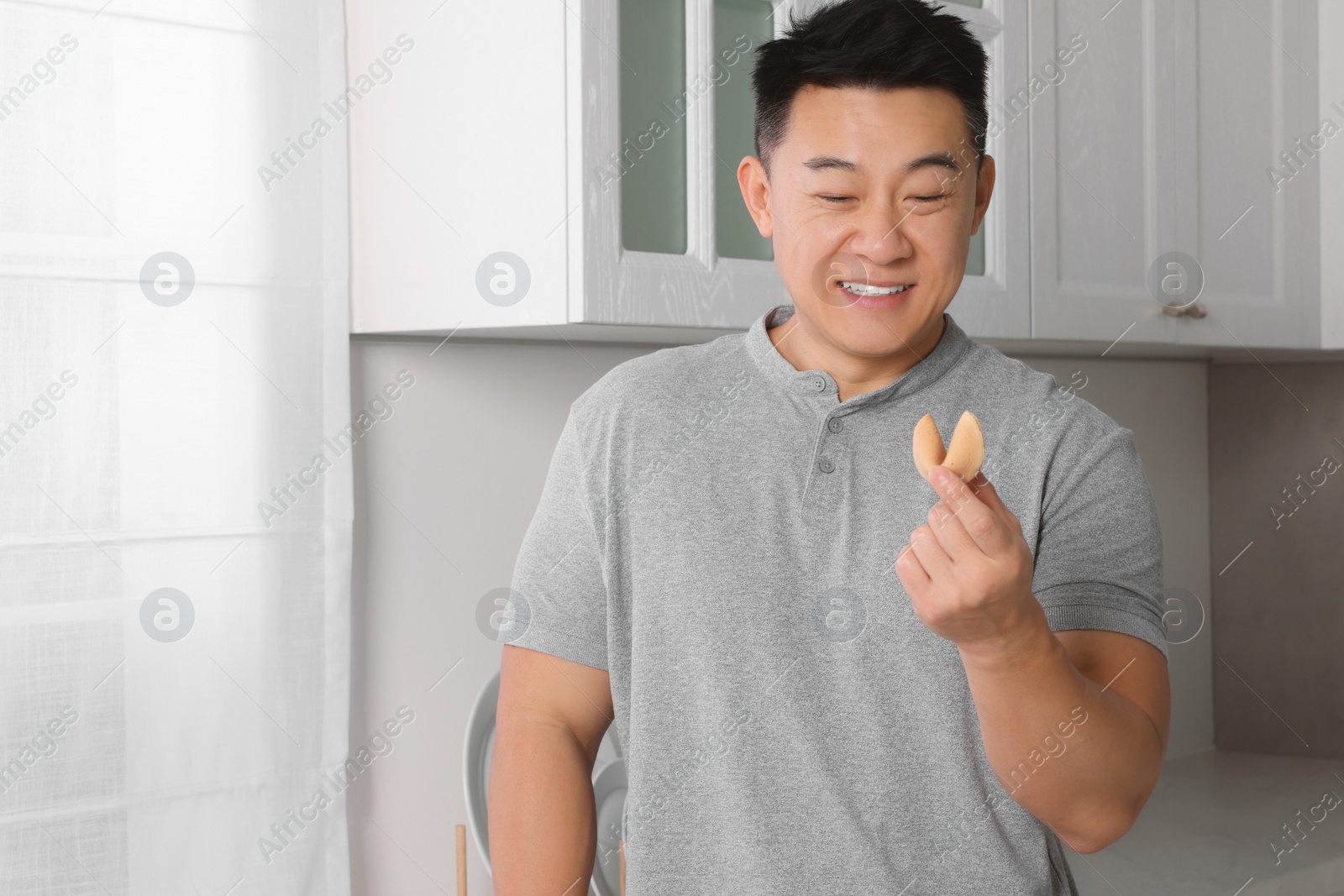 Photo of Happy asian man holding tasty fortune cookie with prediction indoors