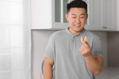 Photo of Happy asian man holding tasty fortune cookie with prediction indoors