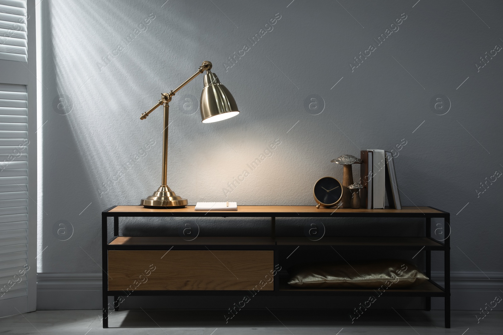 Photo of Stylish lamp, clock and books on wooden cabinet indoors. Interior design