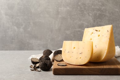 Photo of Delicious cheese and fresh black truffles on grey table. Space for text