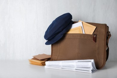 Photo of Postman's hat on bag full of letters and newspapers on white wooden background. Space for text