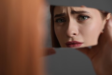 Photo of Young woman looking at herself in shard of broken mirror on grey background, closeup