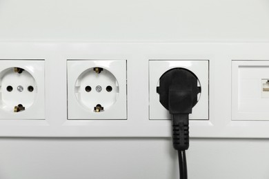 Photo of Power sockets with inserted plug on white wall, closeup. Electrical supply