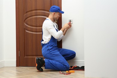 Photo of Professional electrician with screwdriver repairing light switch indoors
