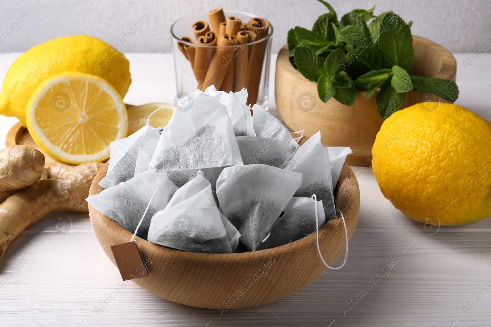 Photo of Tea bags, mint, lemons and ginger on white wooden table, closeup