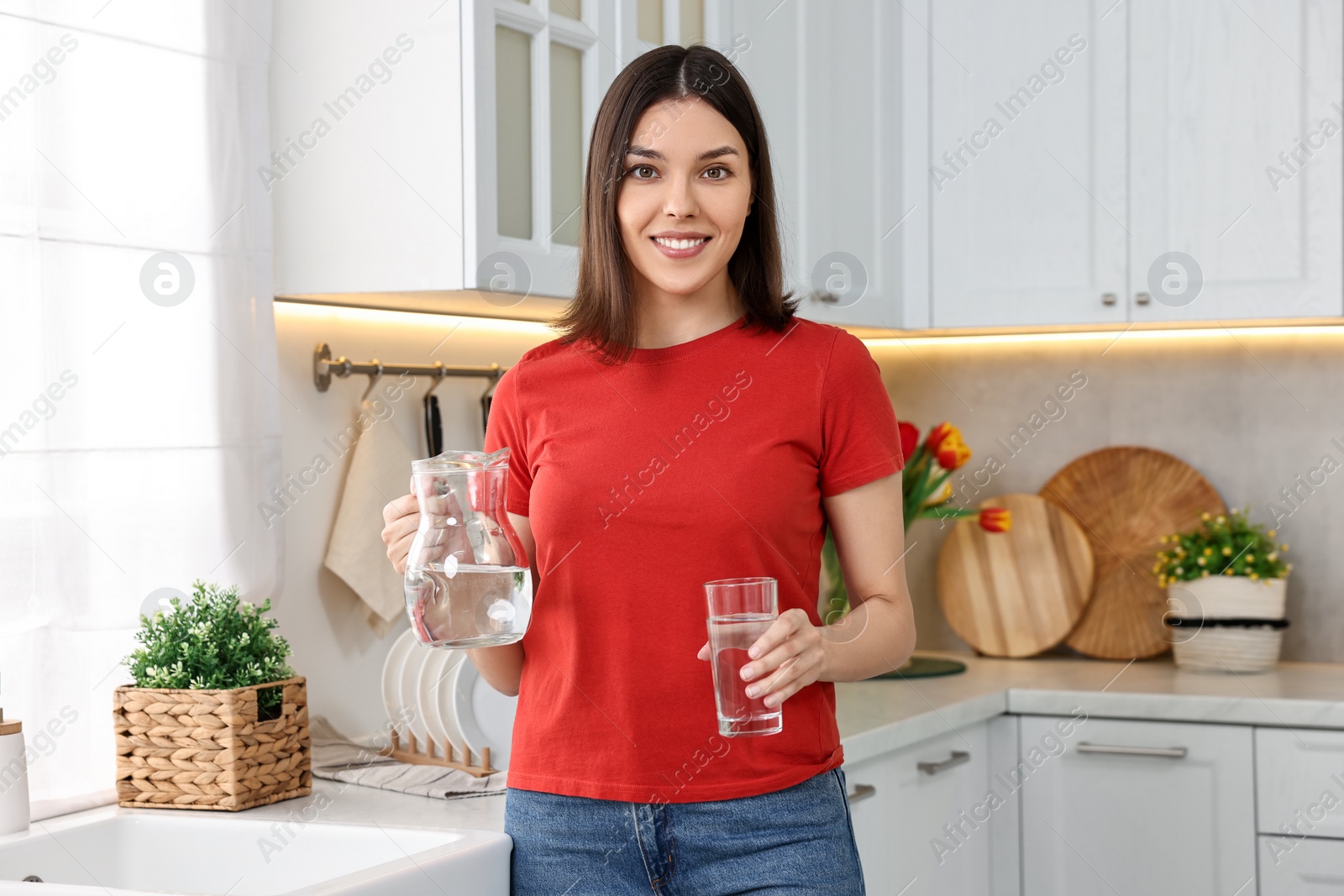 Photo of Young woman with jug and glass of water in kitchen