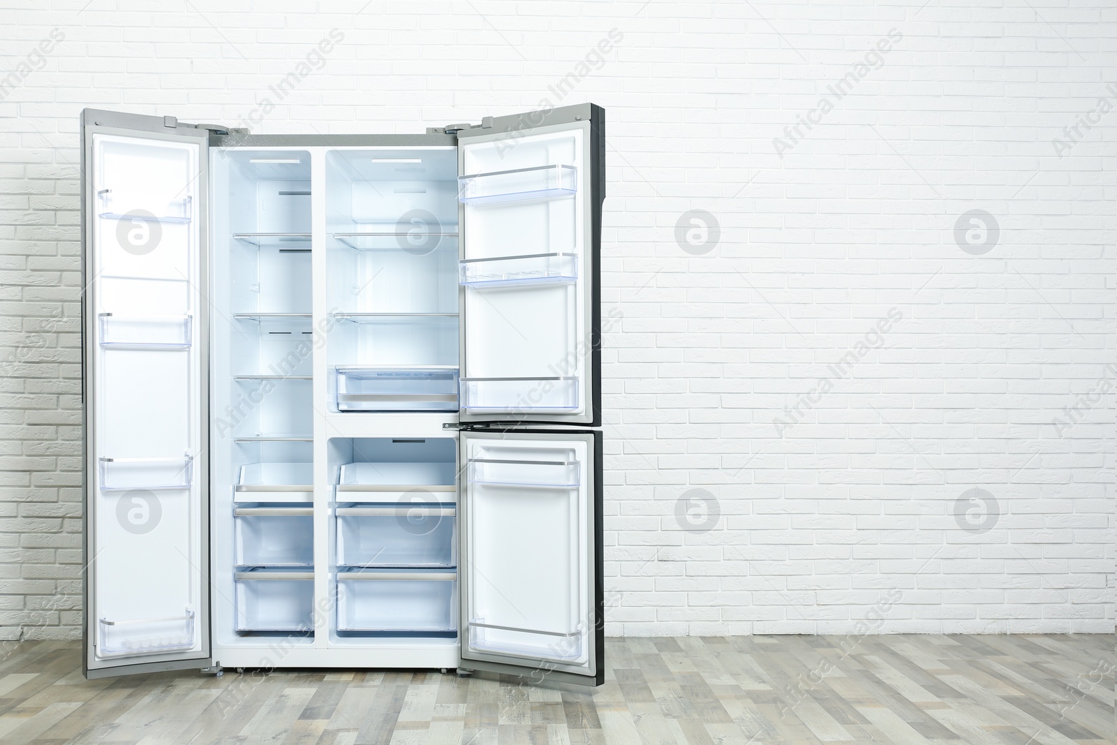 Photo of Modern empty refrigerator near white brick wall, space for text