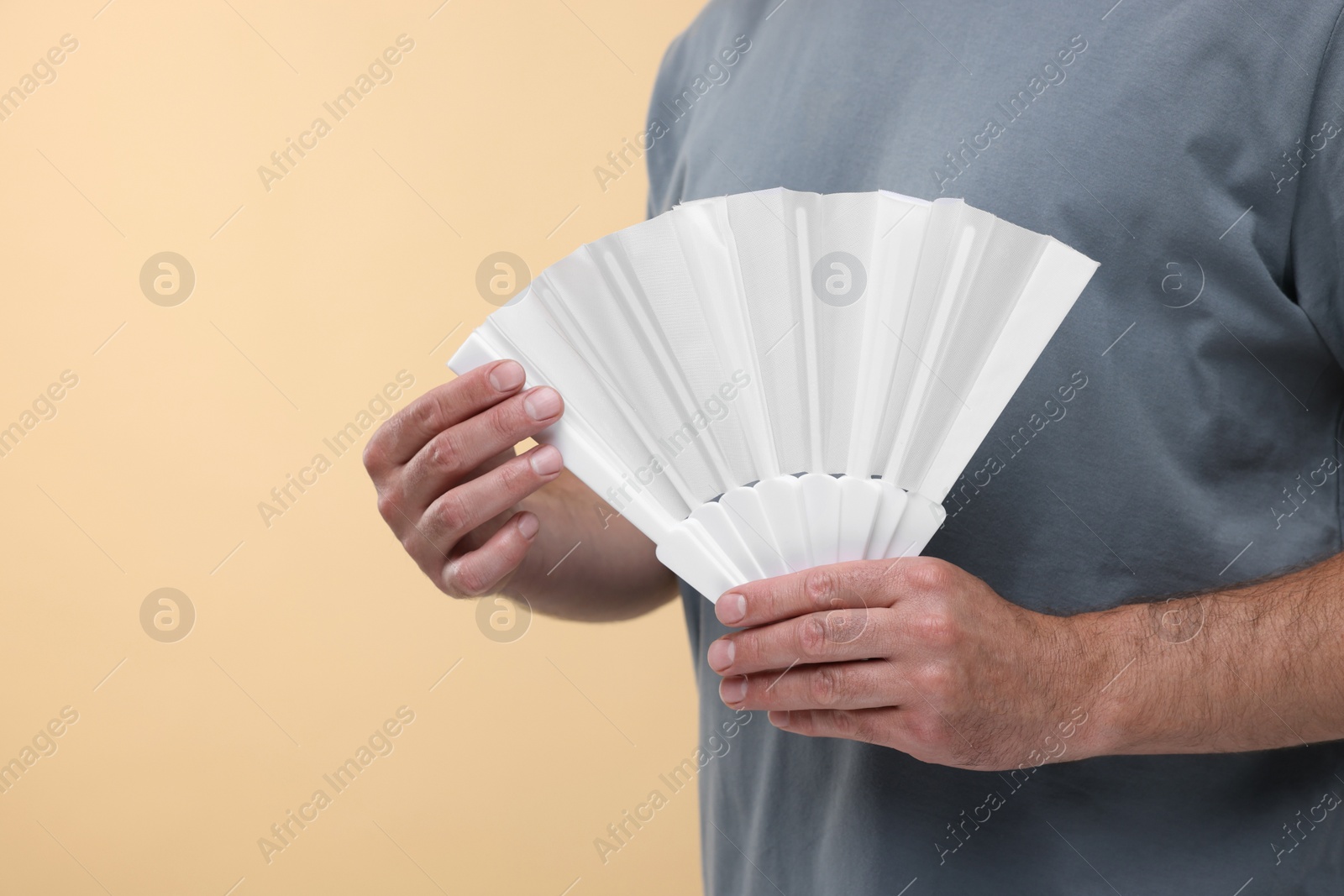 Photo of Man holding hand fan on beige background, closeup. Space for text