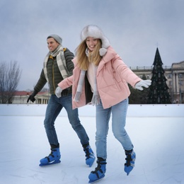 Photo of Happy couple skating along ice rink outdoors