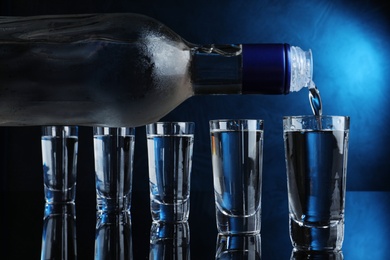 Pouring vodka into shot glass on dark background with blue light