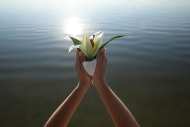 Woman with beautiful lily flower near river, closeup. Nature healing power