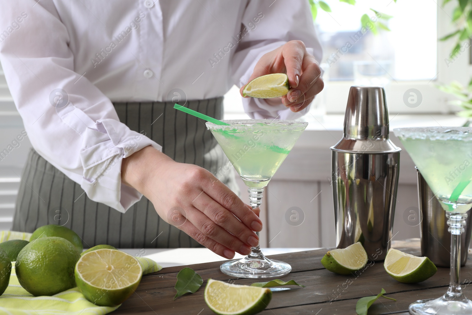 Photo of Bartender squeezing lime juice into glass with delicious Margarita cocktail at wooden table, closeup
