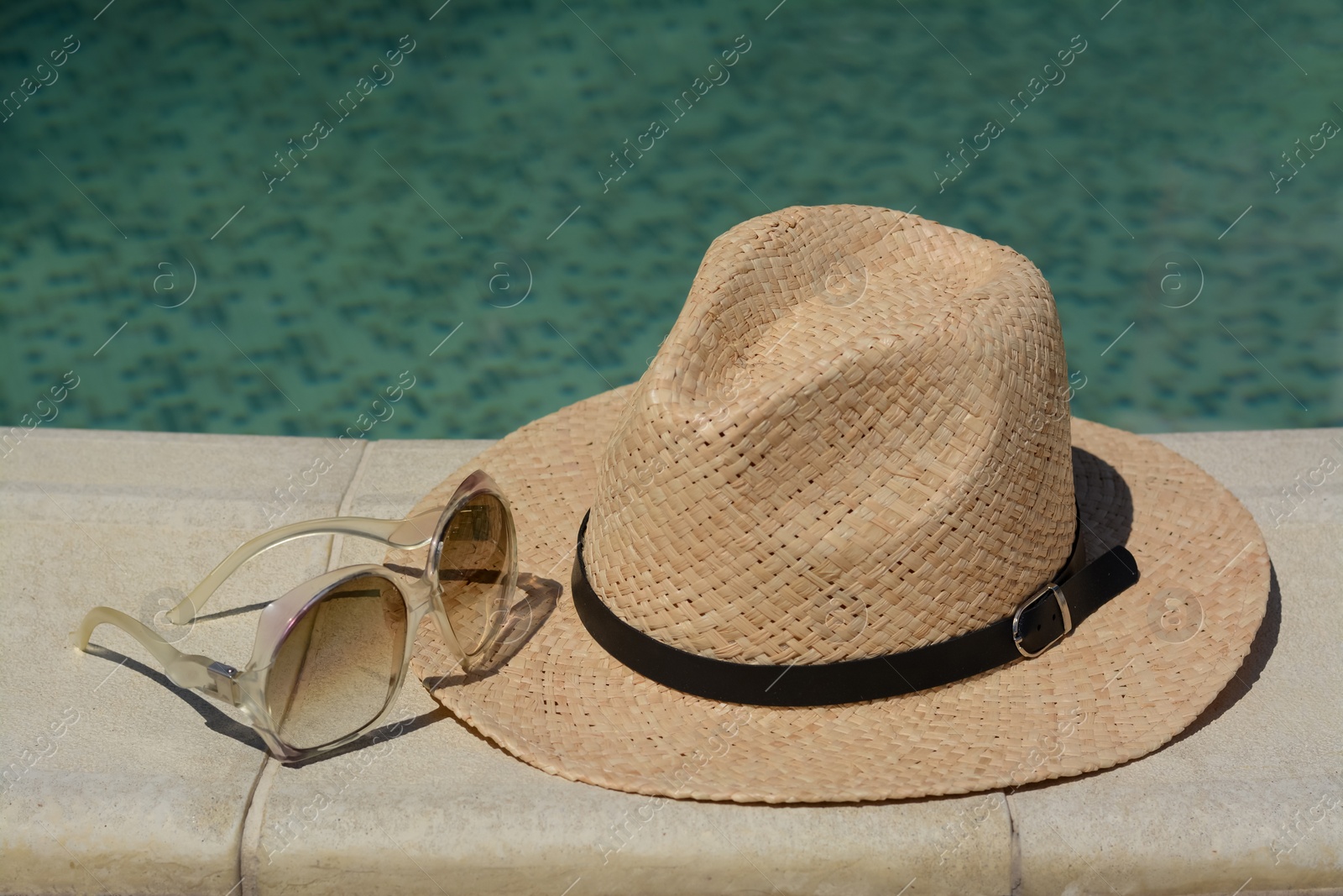 Photo of Stylish hat and sunglasses near outdoor swimming pool on sunny day. Beach accessories