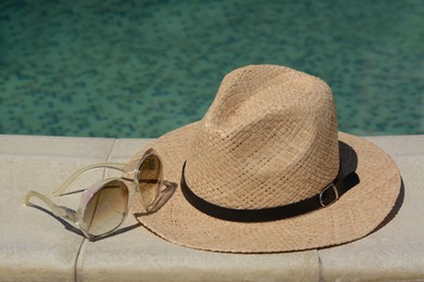 Stylish hat and sunglasses near outdoor swimming pool on sunny day. Beach accessories