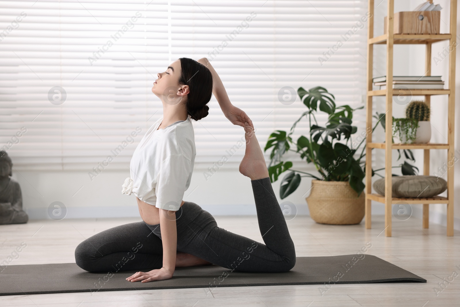 Photo of GIrl practicing one legged king pigeon asana on mat in yoga studio. Eka pada rajakapotasana pose