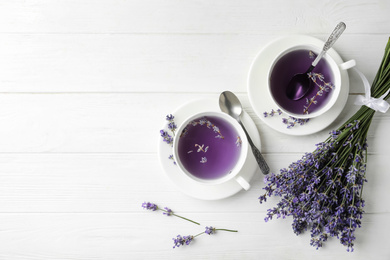 Photo of Fresh delicious tea with lavender and beautiful flowers on white wooden table, flat lay. Space for text