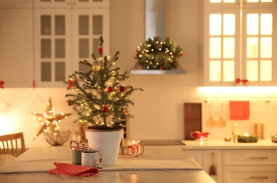 Small Christmas tree decorated with baubles and festive lights in kitchen. Space for text