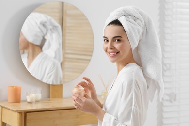 Photo of Beautiful happy woman in stylish bathrobe with cream in bathroom