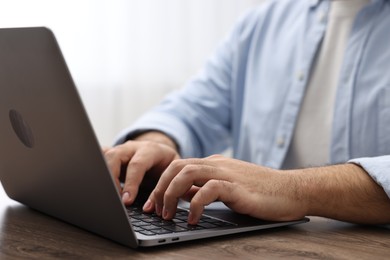 Photo of E-learning. Young man using laptop at wooden table, closeup