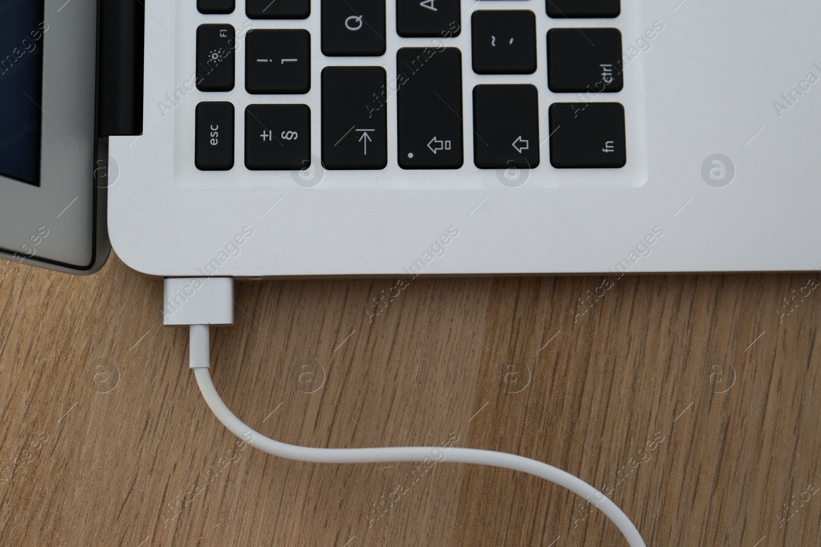 Photo of Modern laptop charging on wooden table, closeup