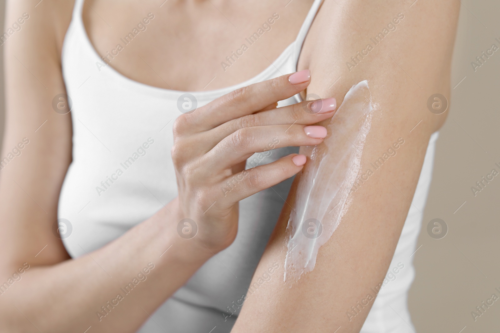Photo of Woman applying body cream onto arm on beige background, closeup